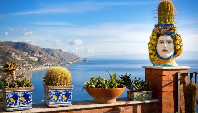 Balcone fiorito con vista sul mare, tra i posti più belli della Sicilia. Cactus e vasi decorati con teste di moro.