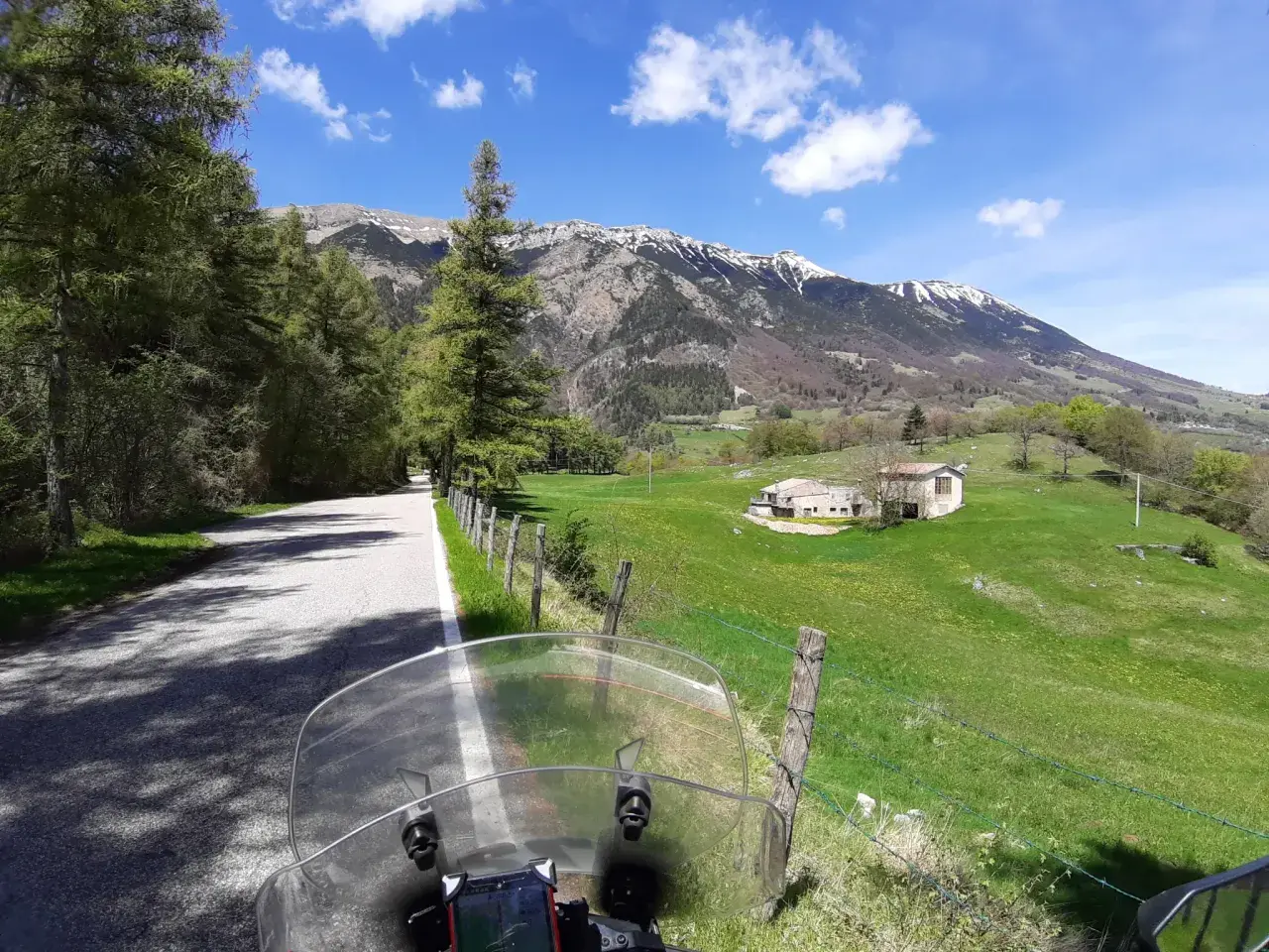 Strada di montagna, un'avventura in moto verso la punta veleno. Paesaggio verdeggiante, montagne innevate e cielo azzurro.