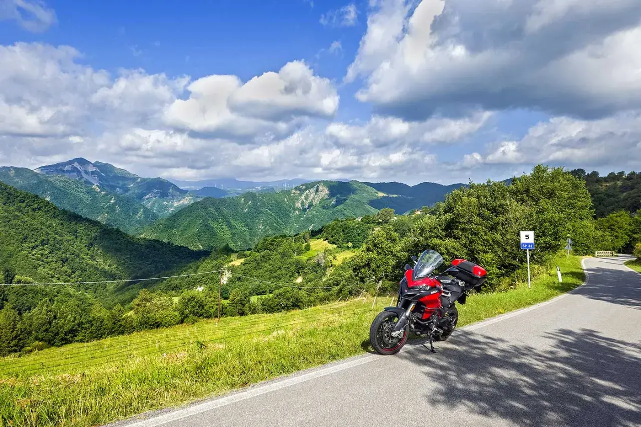 Ducati rossa ferma sul ciglio della strada statale 67, con un panorama mozzafiato di colline verdi e cielo azzurro.