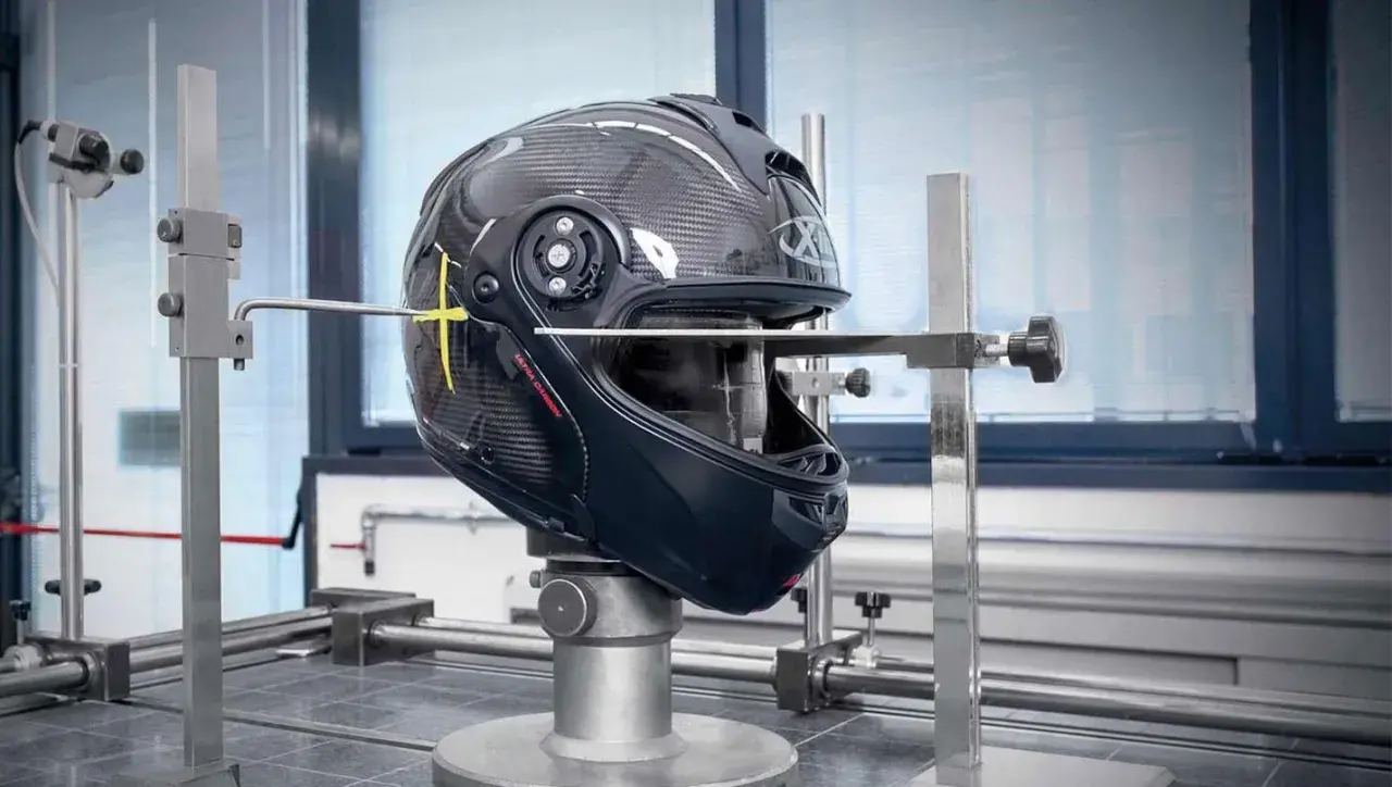 Casco da moto in carbonio sottoposto a test per l'omologazione, con strumenti di misurazione che ne verificano la resistenza e la sicurezza.