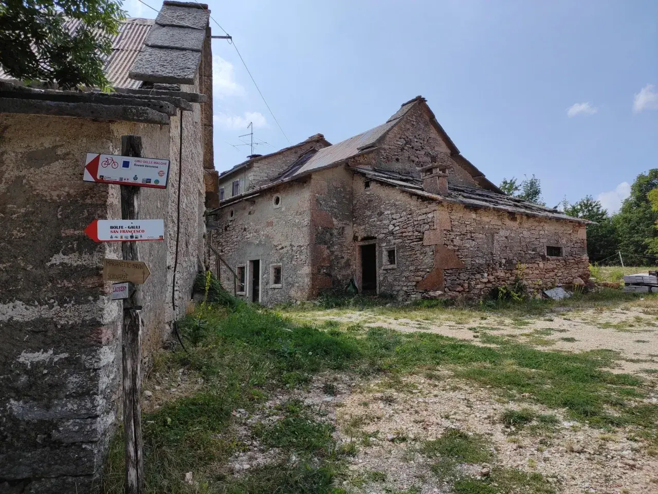 Un vecchio parparo in pietra, con tetto in lamiera e tegole, mostra cartelli per sentieri escursionistici e ciclabili.