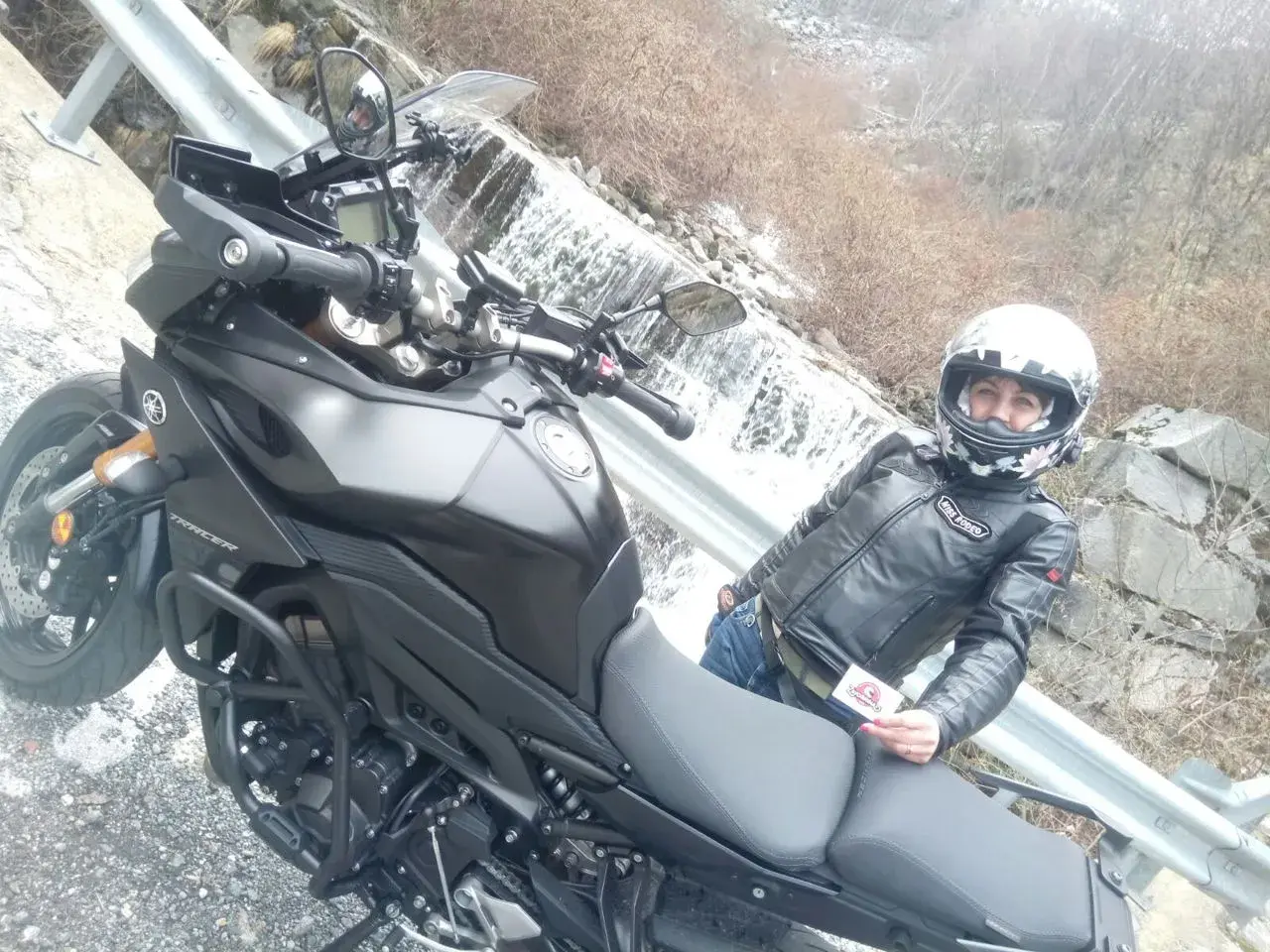 Panoramica Zegna moto con motociclista in giacca di pelle, accanto a una cascata.