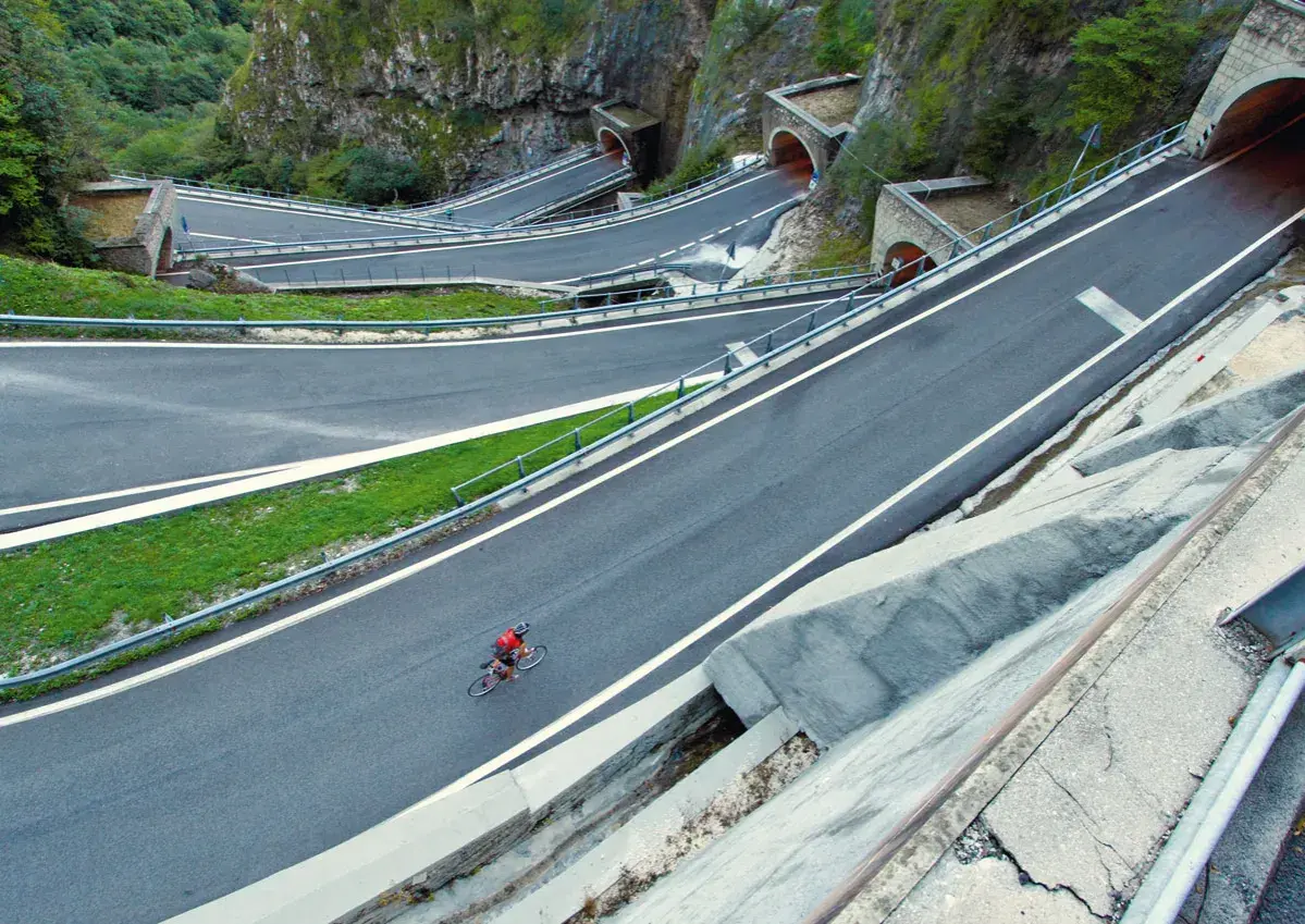 Ciclista solitario affronta i tornanti del passo Bidibidì, tra gallerie scavate nella roccia e panorami mozzafiato.