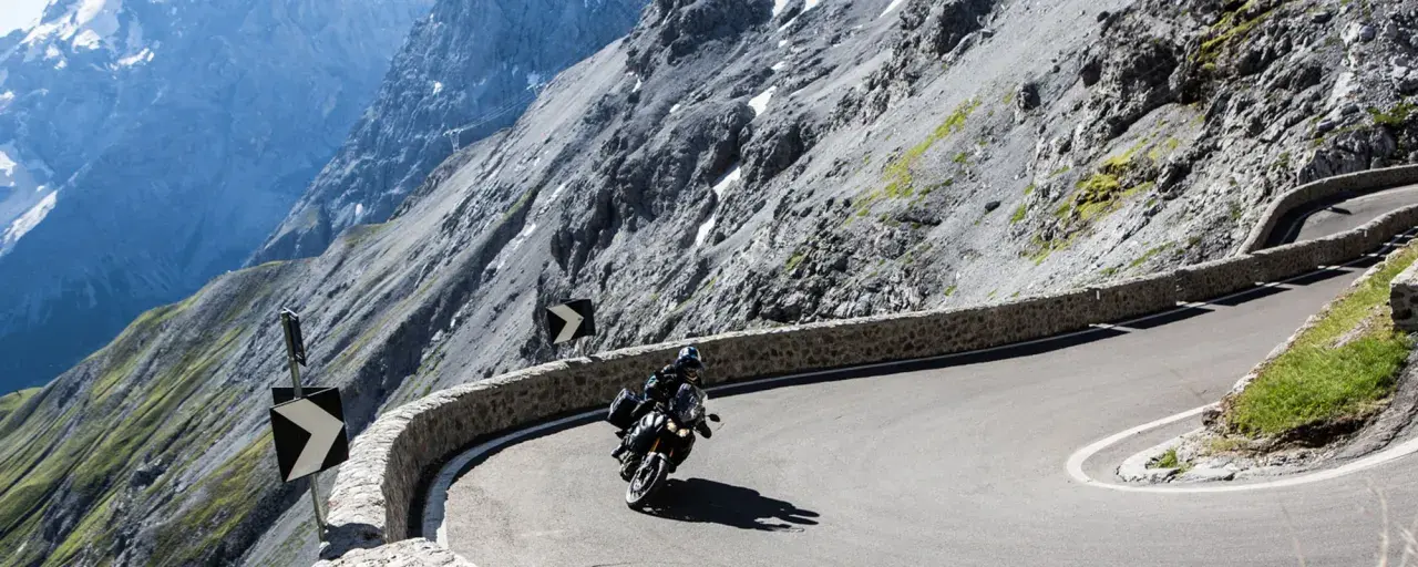 Motociclista affronta tornanti mozzafiato tra le montagne del Trentino, vicino a Merano.