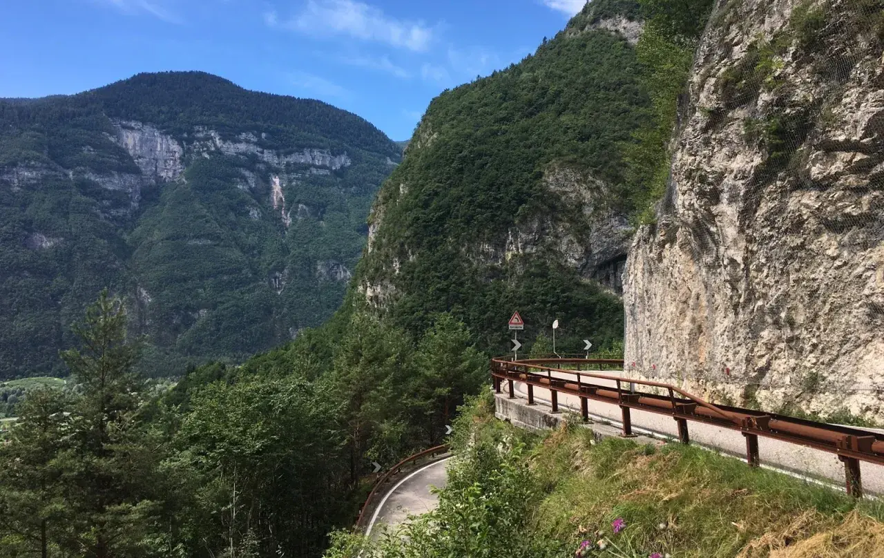 Strada panoramica sul Passo Manghen, con montagne verdi e un cielo azzurro.