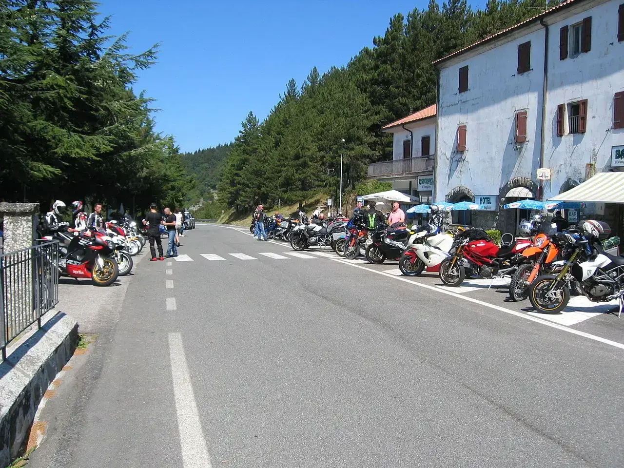 Gruppo di motociclisti in sosta lungo la strada statale 67 Tosco Romagnola, con moto parcheggiate e un hotel sullo sfondo.