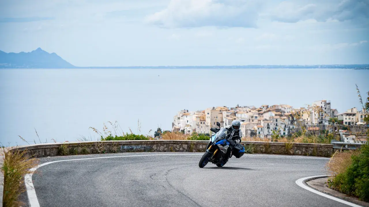 Motociclista in curva su strada panoramica, con il mare e il borgo di Sperlonga sullo sfondo. Un viaggio da Terracina a Sperlonga.