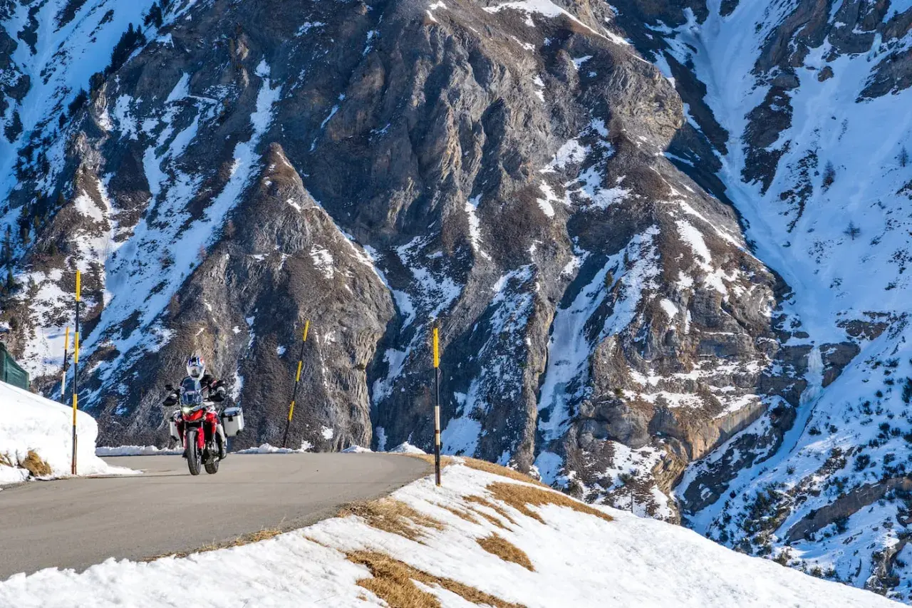 Motociclista su strada innevata tra le montagne, un viaggio da Bolzano a Livigno.