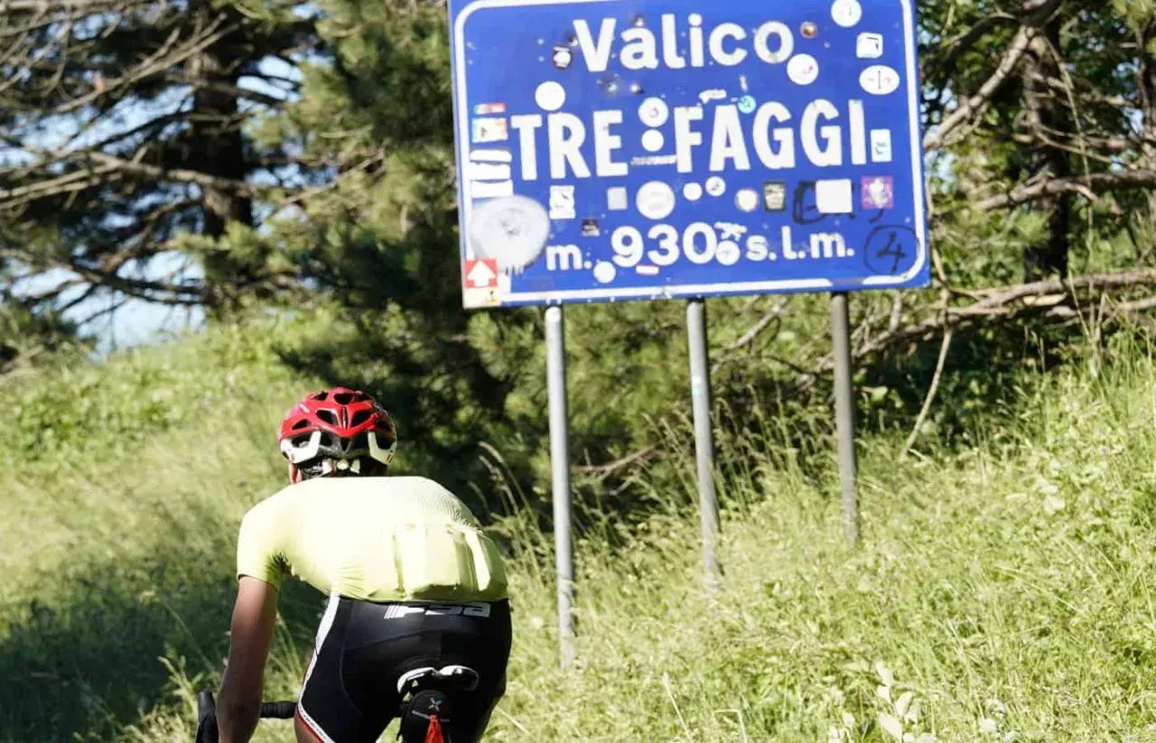 Ciclista in cima al valico Tre Faggi, 930 metri sul livello del mare, tra alberi e erba alta.