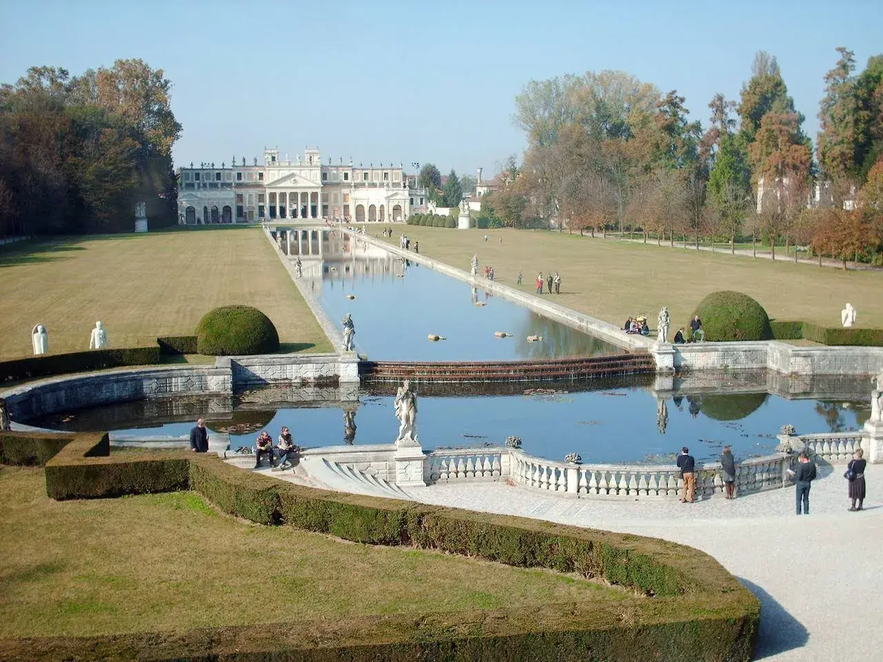 Un'imponente villa con un lungo specchio d'acqua e giardini curati, che ricorda le ville palladiane.