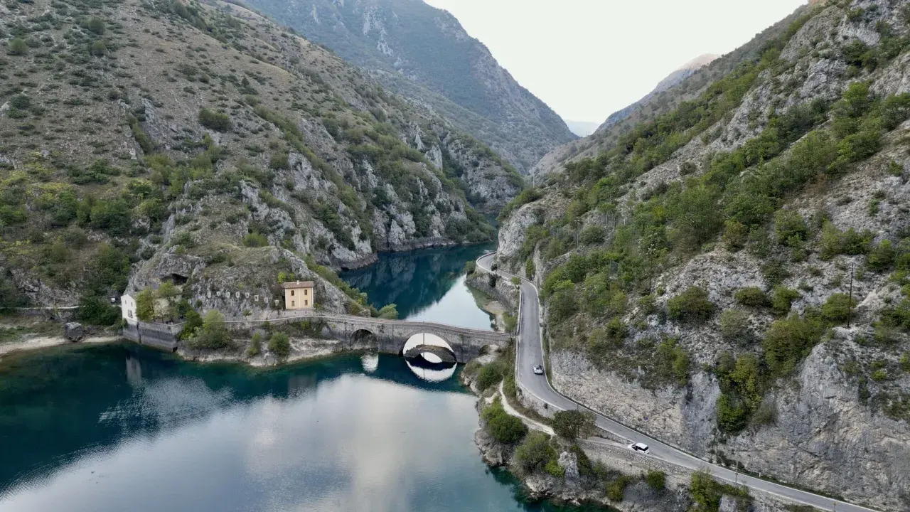 Le gole del Sagittario a Scanno, con il lago turchese, il ponte ad arco e la strada panoramica che serpeggia tra le montagne.