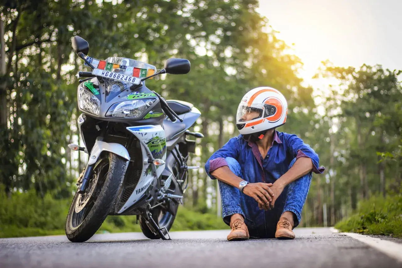 Giovane con casco arancione e bianco, seduto accanto alla sua moto. Spera di allargare il casco stretto per un viaggio più comodo.