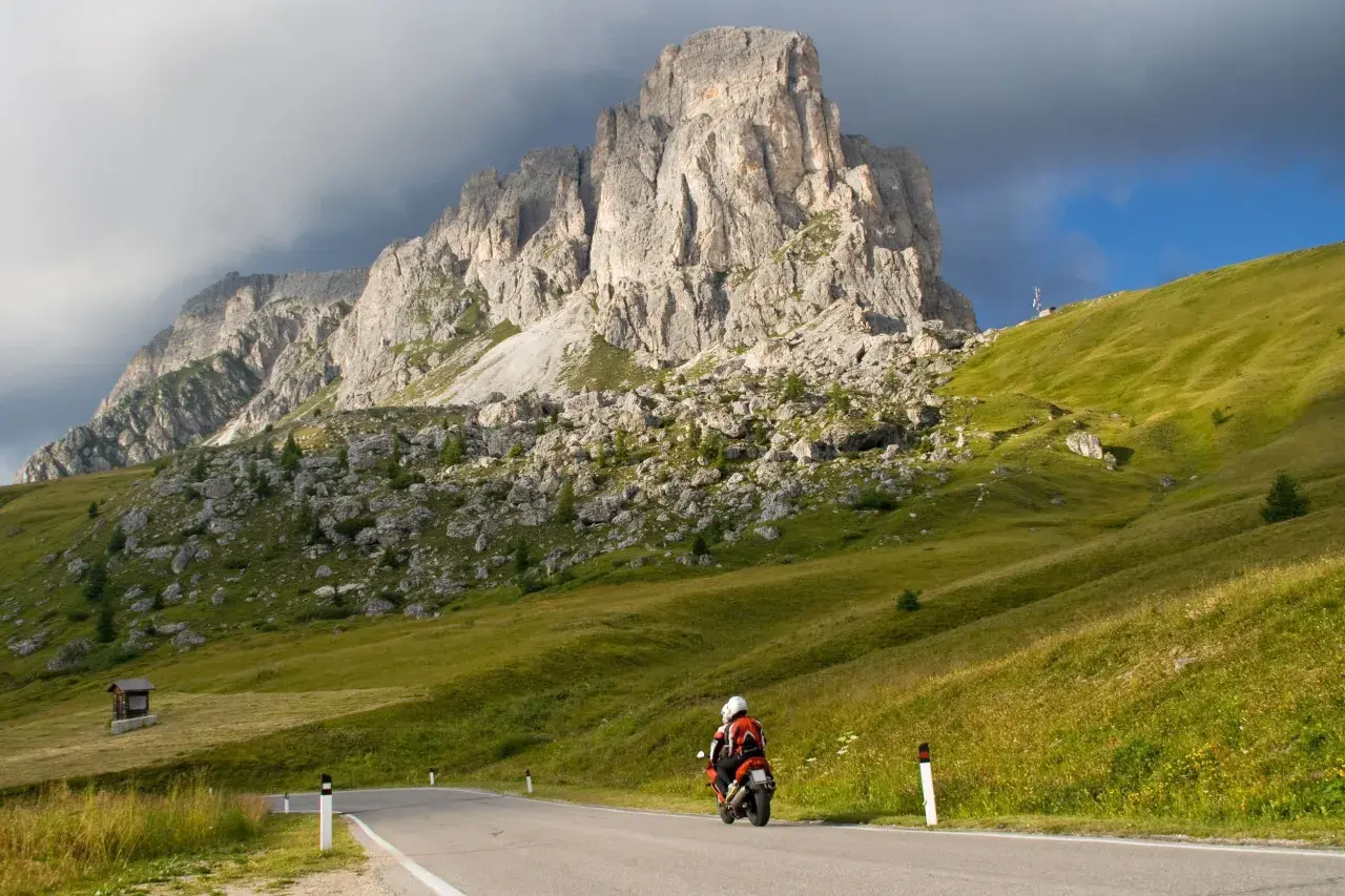 Motociclista in viaggio verso il passo del cerro, con imponenti montagne sullo sfondo e verdi pendii erbosi.