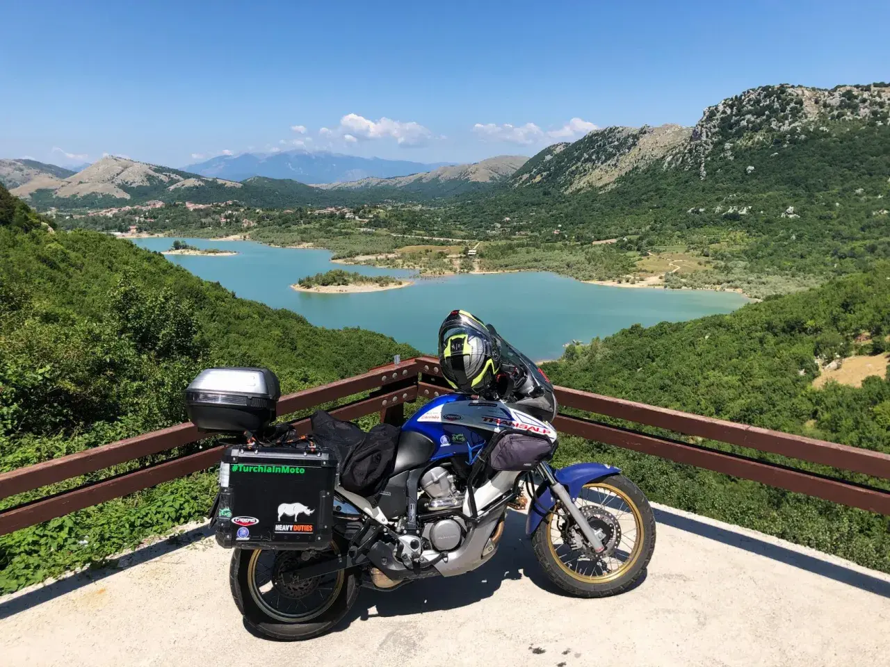 Moto pronta per esplorare gli Appennini, con un lago turchese e montagne verdi sullo sfondo. #AppenniniInMoto