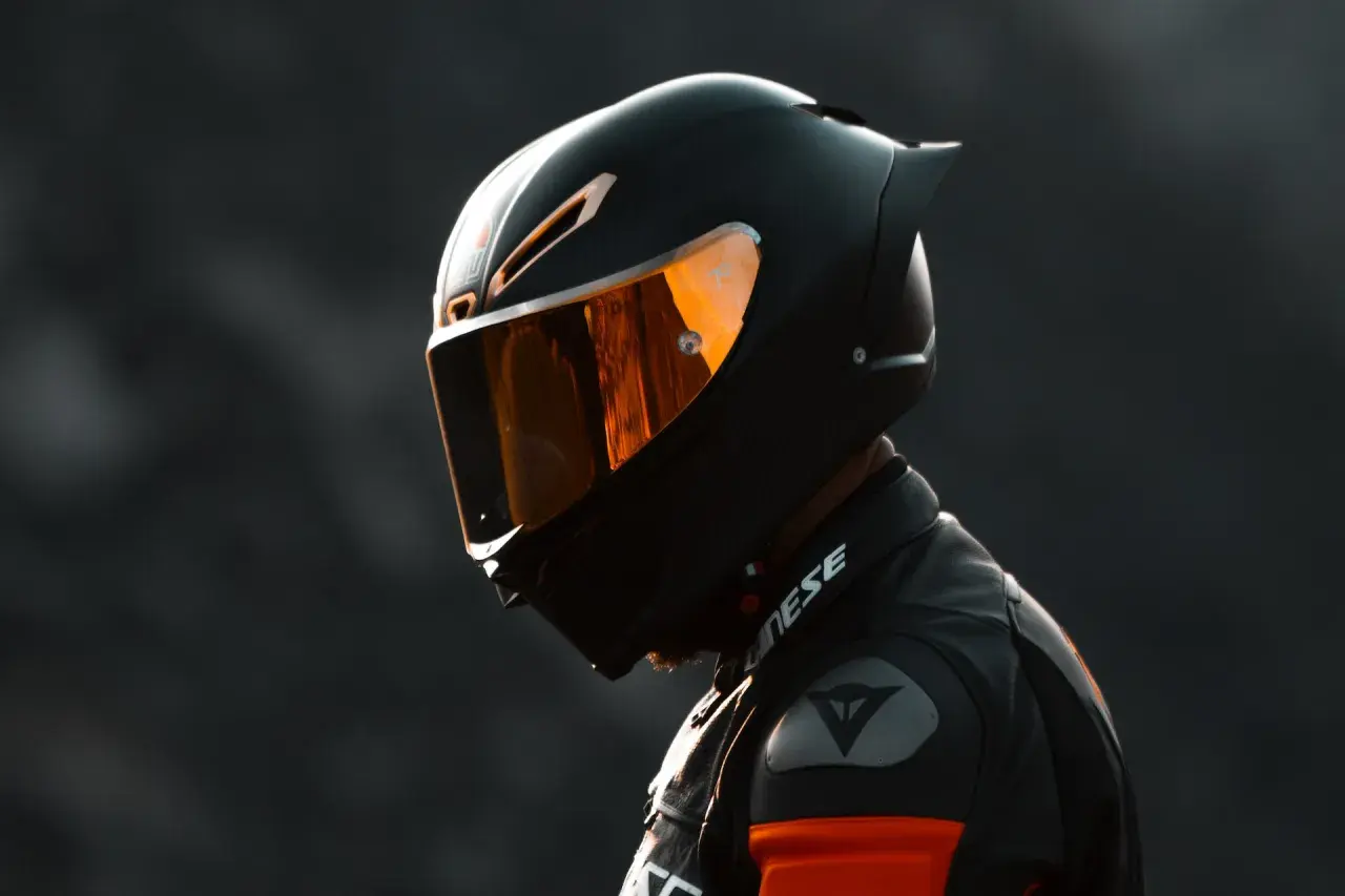 Un motociclista indossa un casco integrale nero con visiera arancione riflettente, pronto per la pista.