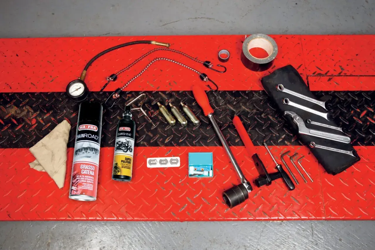 Kit di attrezzi da portare in moto: grasso catena, pulitore, chiavi, brugole, compressore portatile e nastro adesivo.