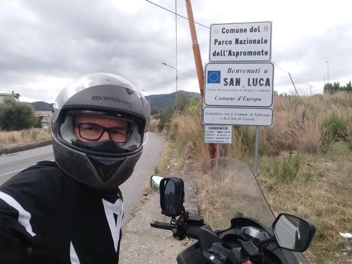 Sila in moto, selfie con casco e giacca da motociclista, vicino ai cartelli del Parco Nazionale dell'Aspromonte e di San Luca.