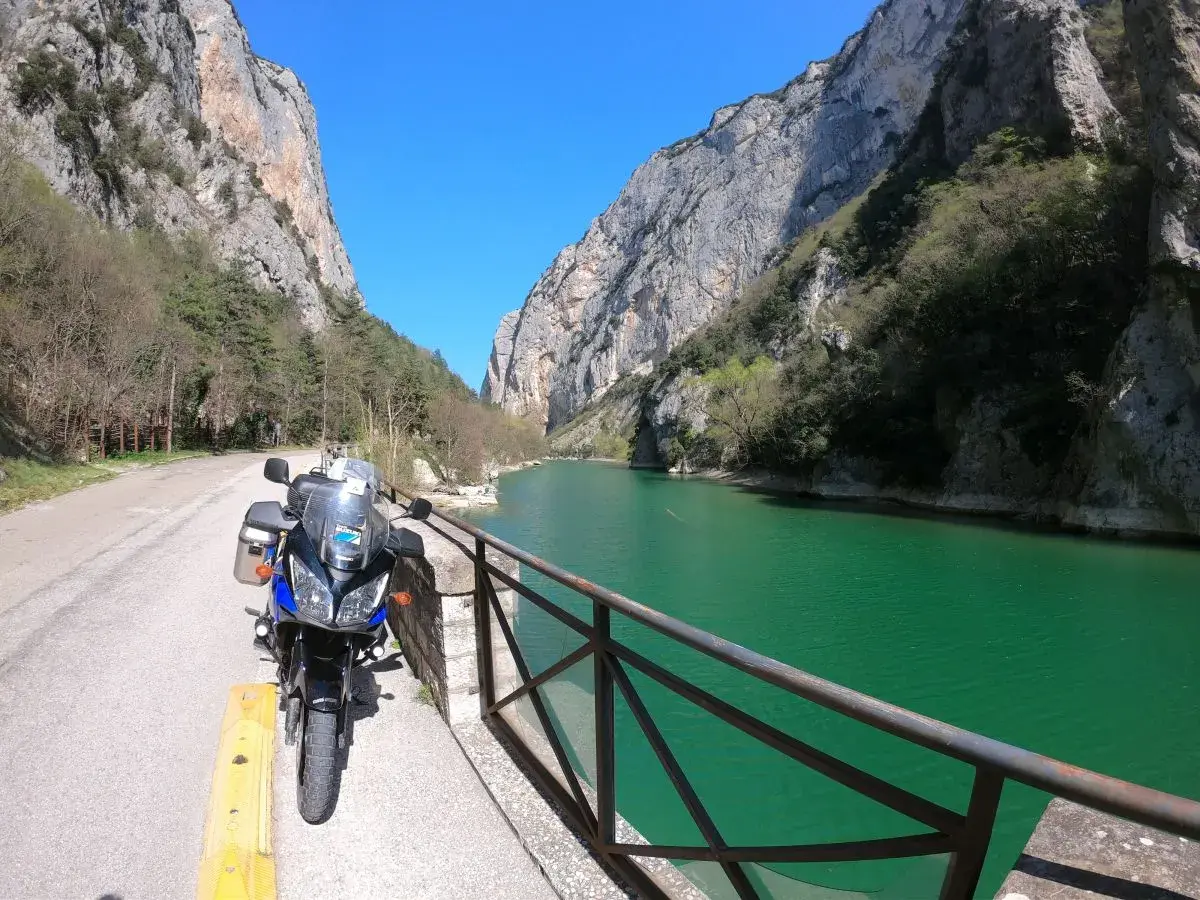 Moto parcheggiata lungo la strada panoramica delle Gole del Furlo, con il fiume color smeraldo e le imponenti pareti rocciose.
