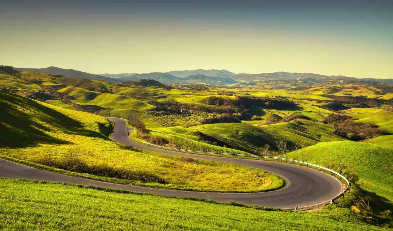 Strada volterrana serpeggiante tra dolci colline verdi sotto un cielo limpido.