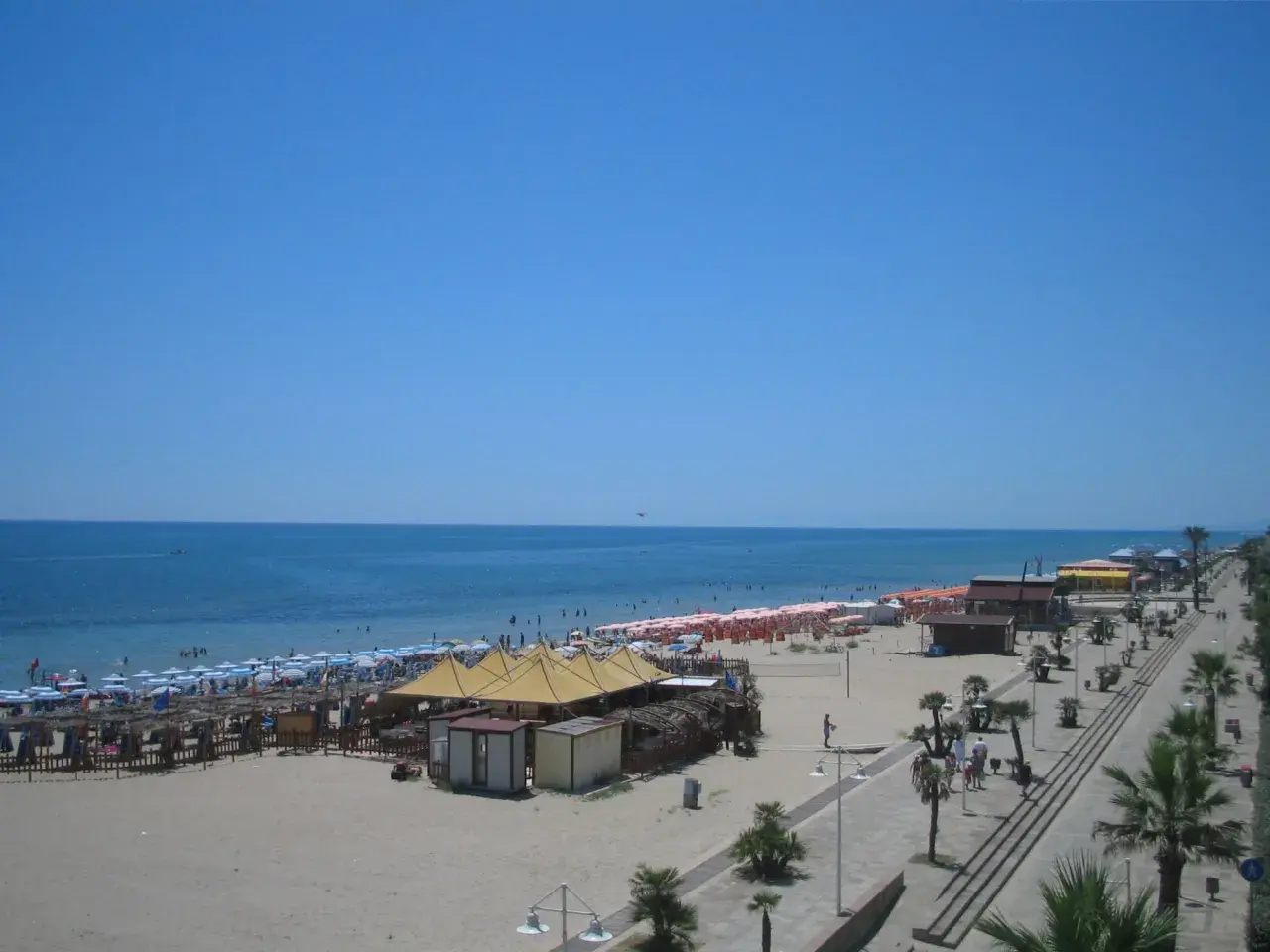 Spiaggia affollata a Metaponto, dove si trova un lido con ombrelloni, lettini e stabilimenti balneari. Il mare azzurro e il cielo limpido invitano al relax.