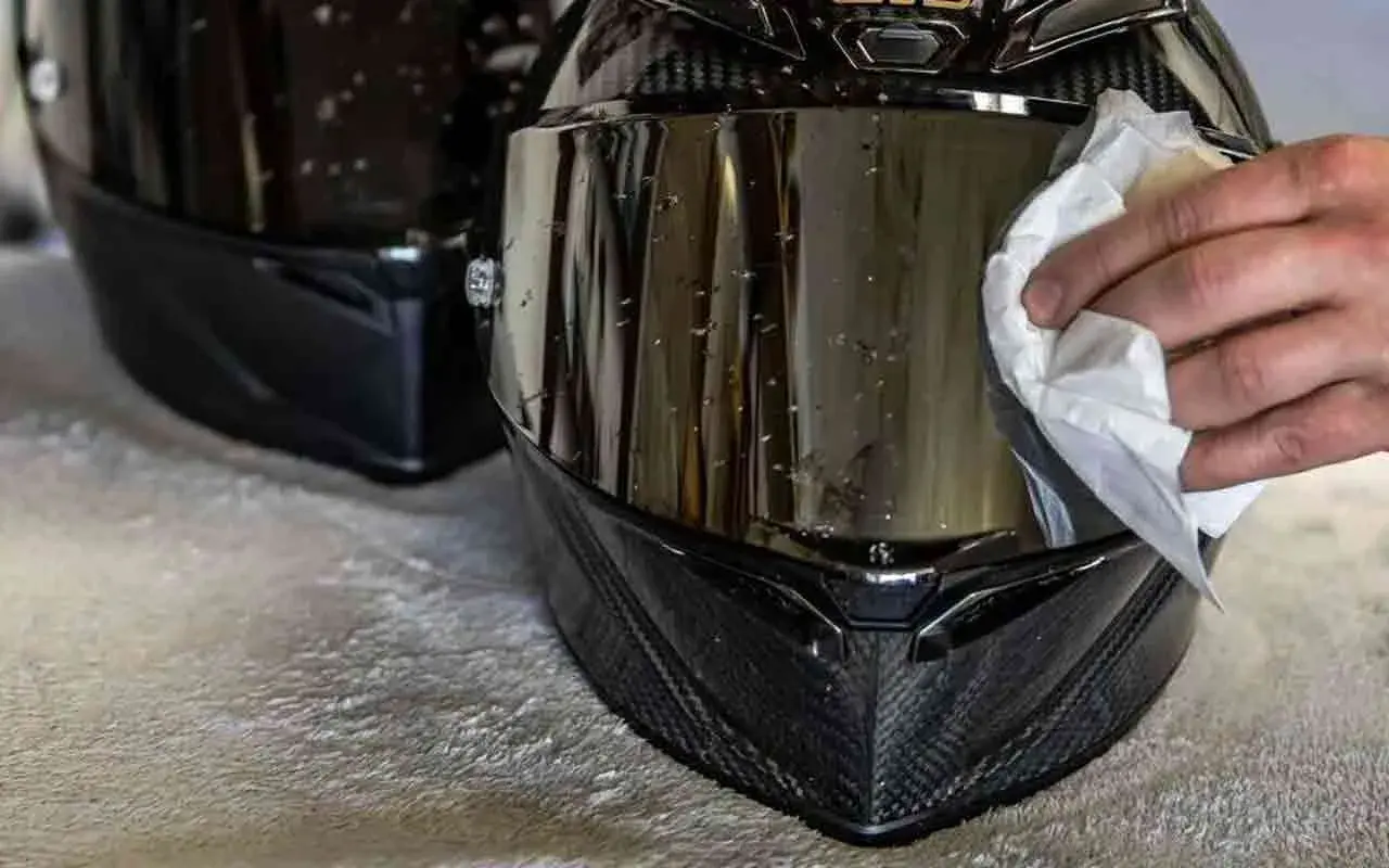 Mano che pulisce la visiera del casco con un panno bianco, rimuovendo insetti e sporco per una guida sicura.
