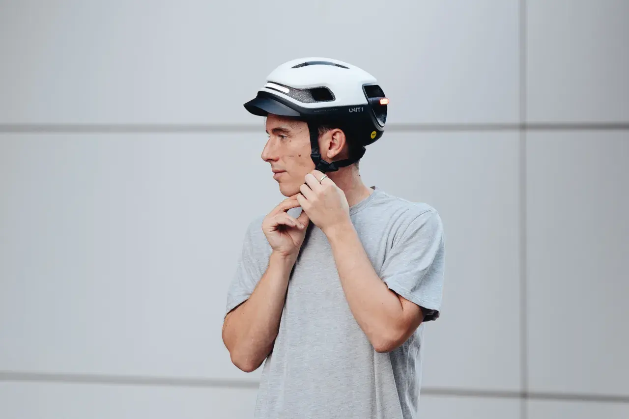 Uomo con casco bianco e nero, che regola gli spallacci. Le taglie caschi sono fondamentali per la sicurezza.