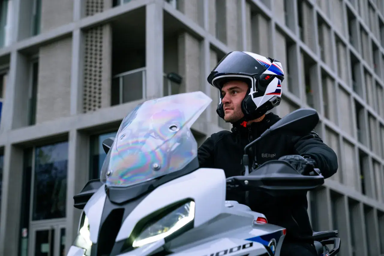 Motociclista con casco modulare, che può essere jet o integrale, pronto a partire con la sua moto davanti a un edificio moderno.