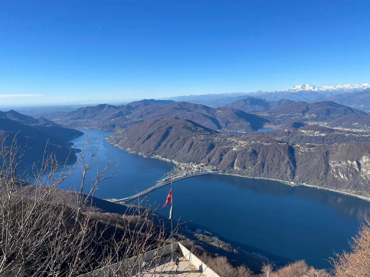 Vista mozzafiato dal balcone d'Italia. Un lago blu intenso abbraccia montagne boscose, con un ponte che attraversa le acque. Perfetto per un viaggio in moto.