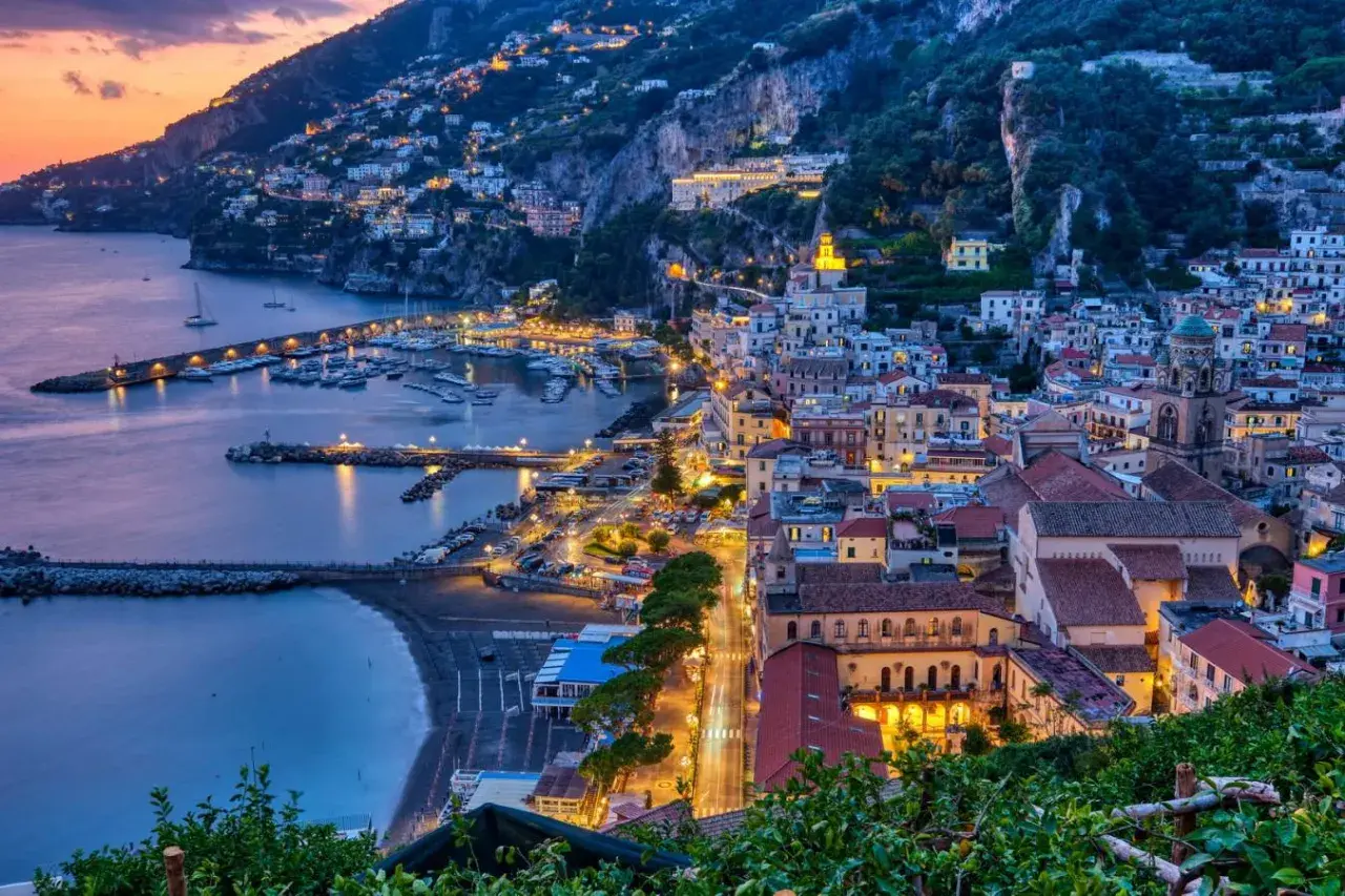 Le luci illuminano le case aggrappate alla costa e il porto turistico. Le strade costiera amalfitana prendono vita al tramonto.