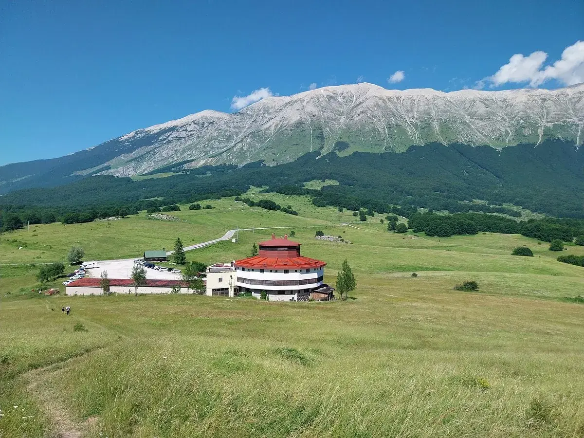 Edificio circolare con tetto rosso e montagne sullo sfondo, al passo San Leonardo.