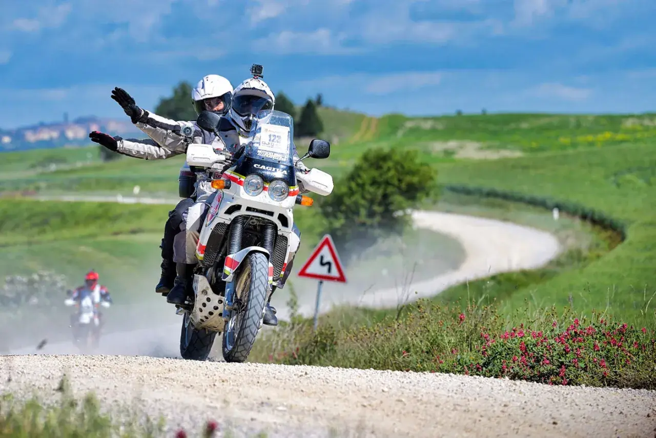 Coppia in moto su sterrato, seguendo una mappa percorso eroica in moto tra colline verdi.
