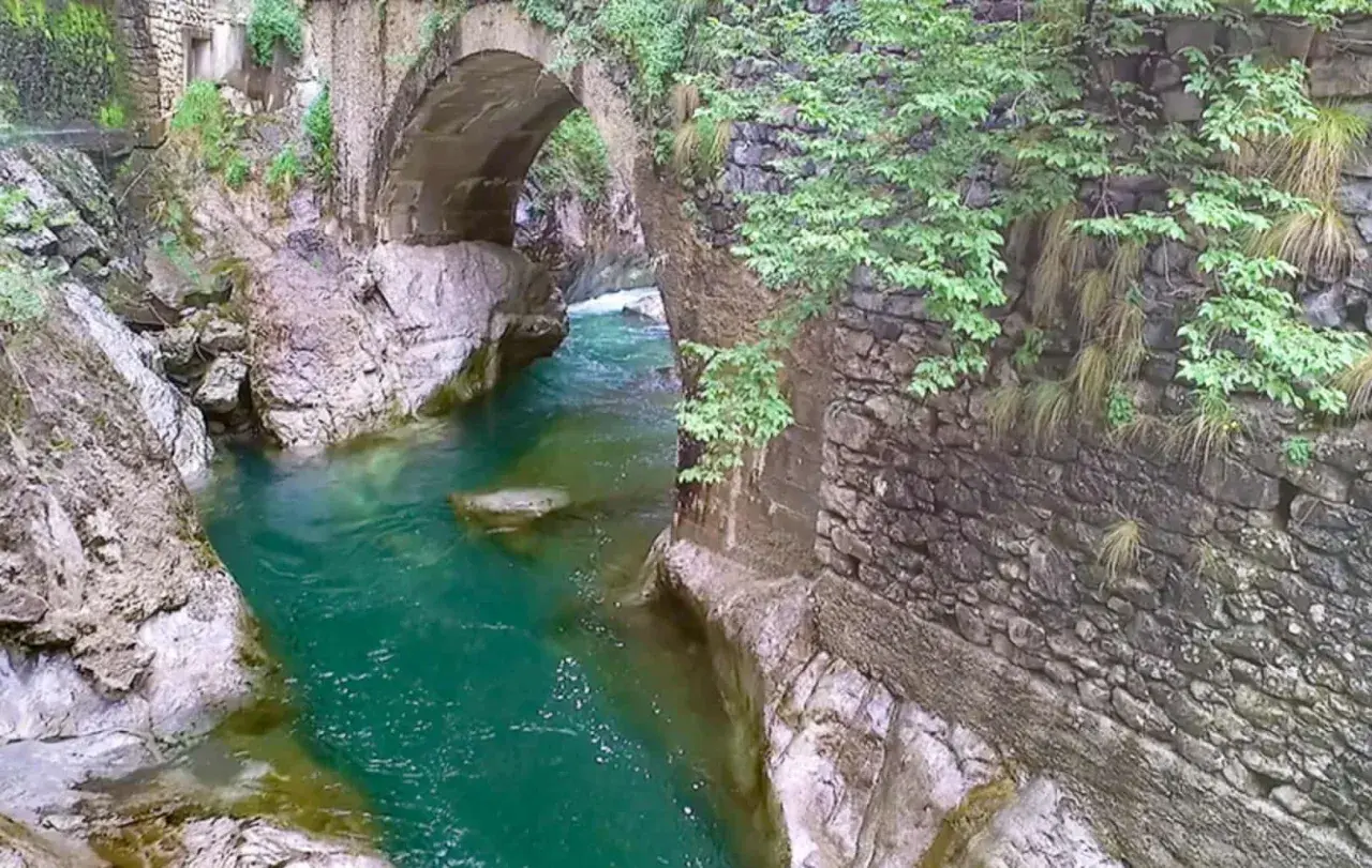 Acqua smeraldo scorre sotto un antico ponte di pietra, creando un'atmosfera suggestiva nell'orrido Val Taleggio.