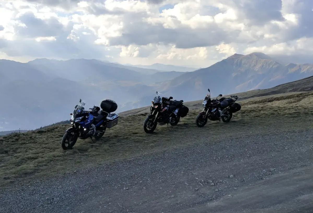 Tre moto attendono al Passo dell'Abetone, con un panorama montano mozzafiato sotto un cielo nuvoloso.