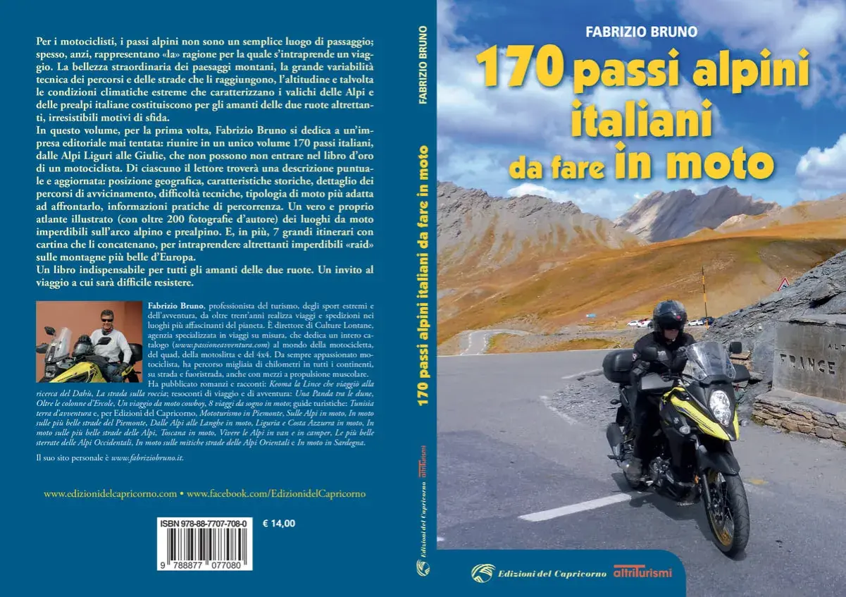 Motociclista in cima a un passo alpino, con montagne sullo sfondo. Un invito a scoprire 170 passi alpini italiani da fare in moto.