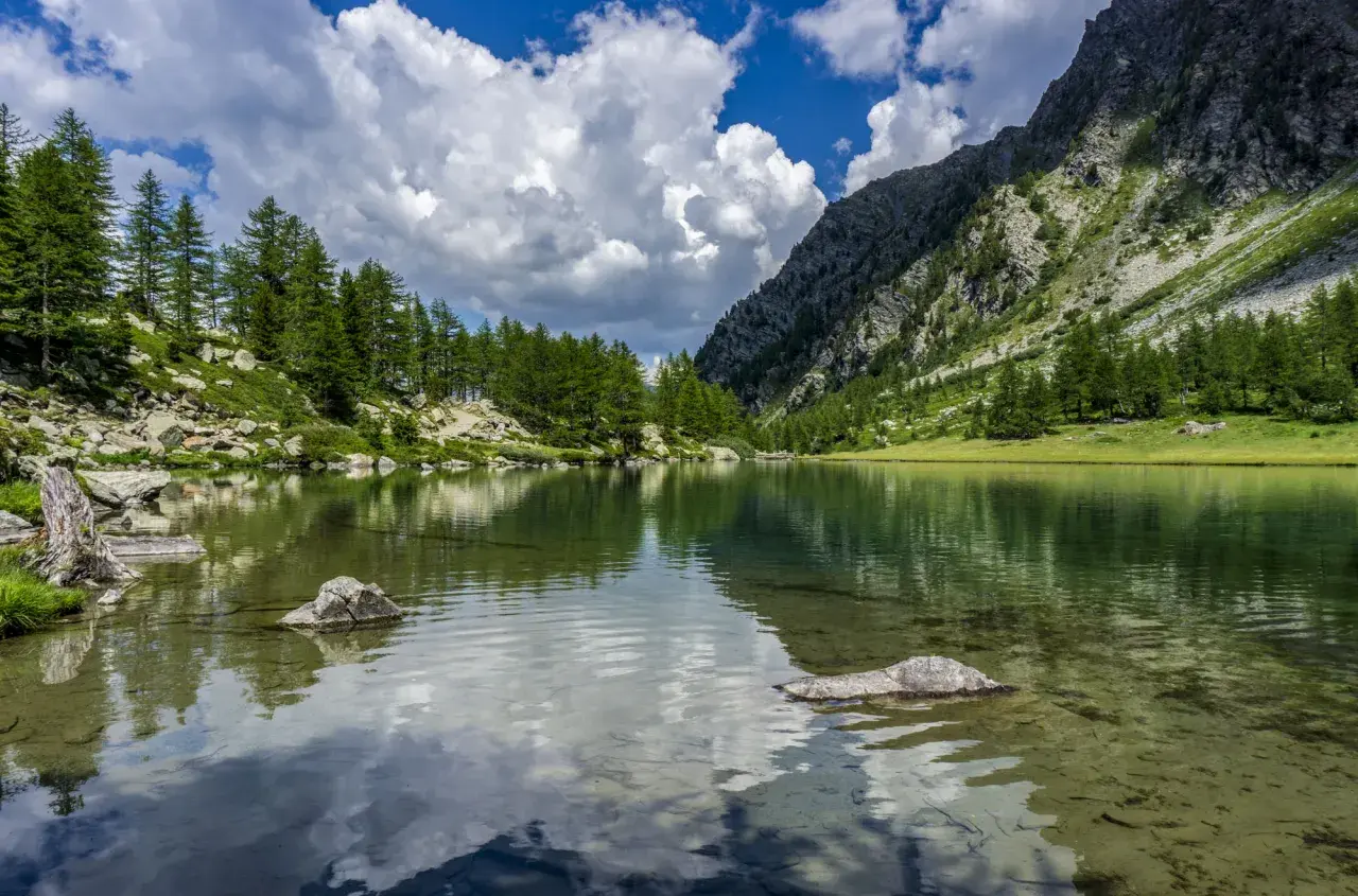 Un lago alpino tranquillo riflette il cielo nuvoloso e le montagne boscose. Un paesaggio mozzafiato dei laghi della Valle d'Aosta.