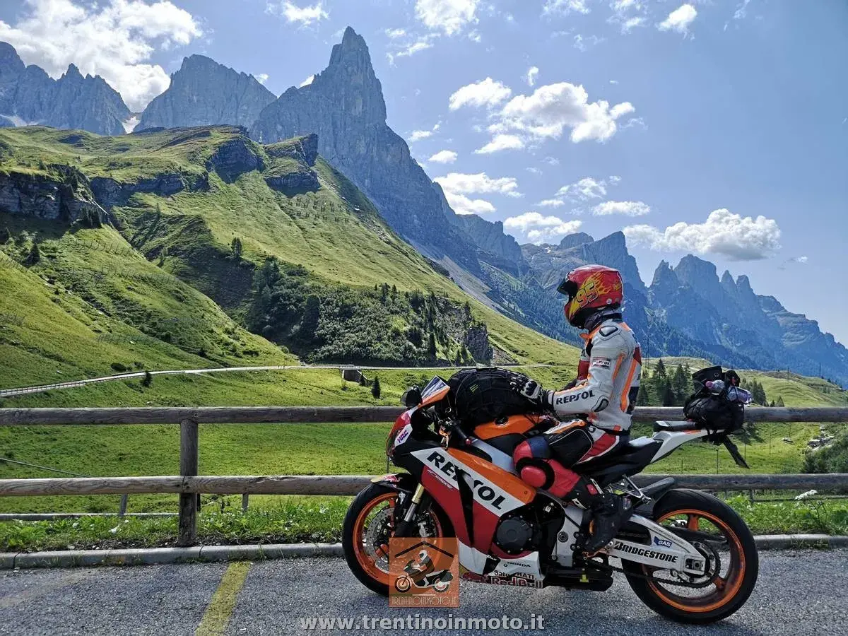 Motociclista in tenuta da gara su una Honda Repsol, con lo sfondo delle maestose vette del Passo Cereda.