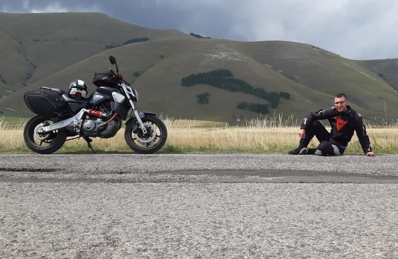 Motociclista in tenuta da gara seduto sul ciglio della strada al passo San Antonio, con la sua moto parcheggiata accanto.