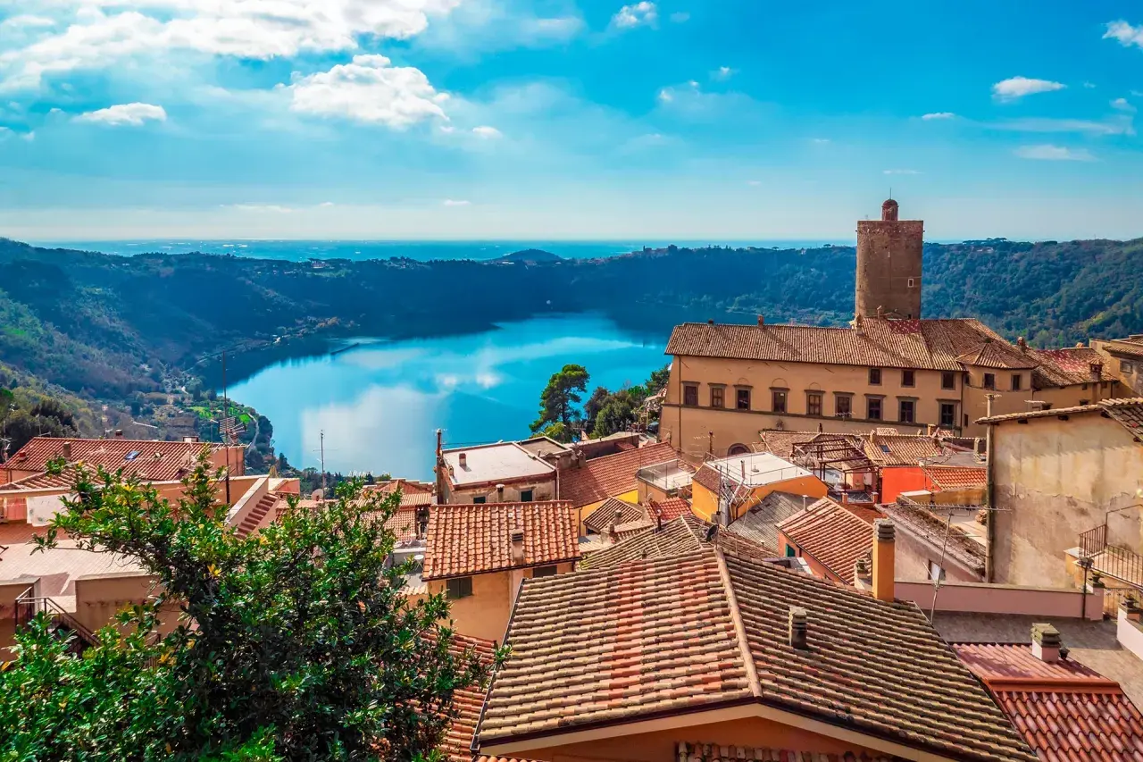 Panoramica dei Castelli Romani in moto: tetti rossi, un lago blu e un cielo terso.