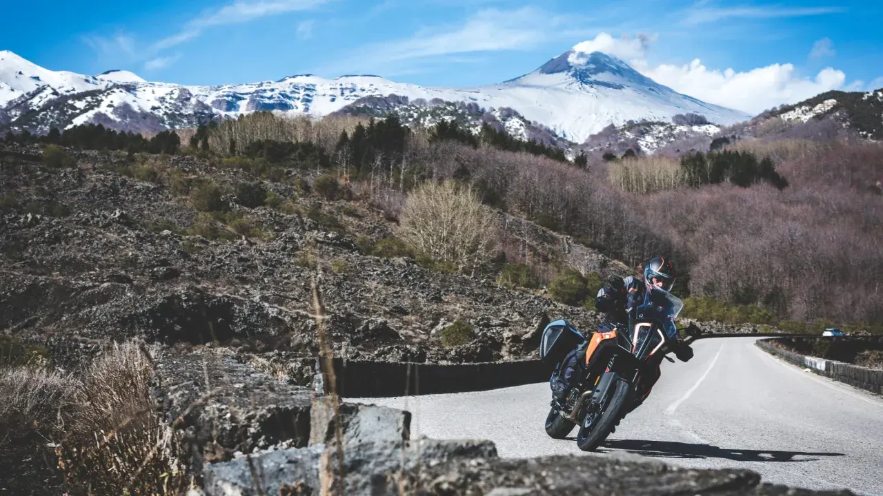 Motociclista su strada mareneve, con vulcano innevato sullo sfondo.