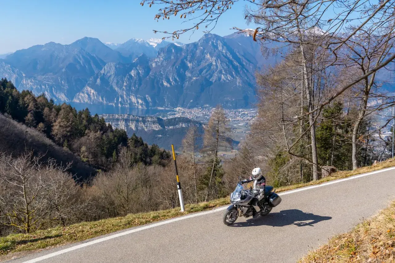 Un motociclista si gode un giro in moto sul Lago di Garda, con montagne maestose e un villaggio sullo sfondo.