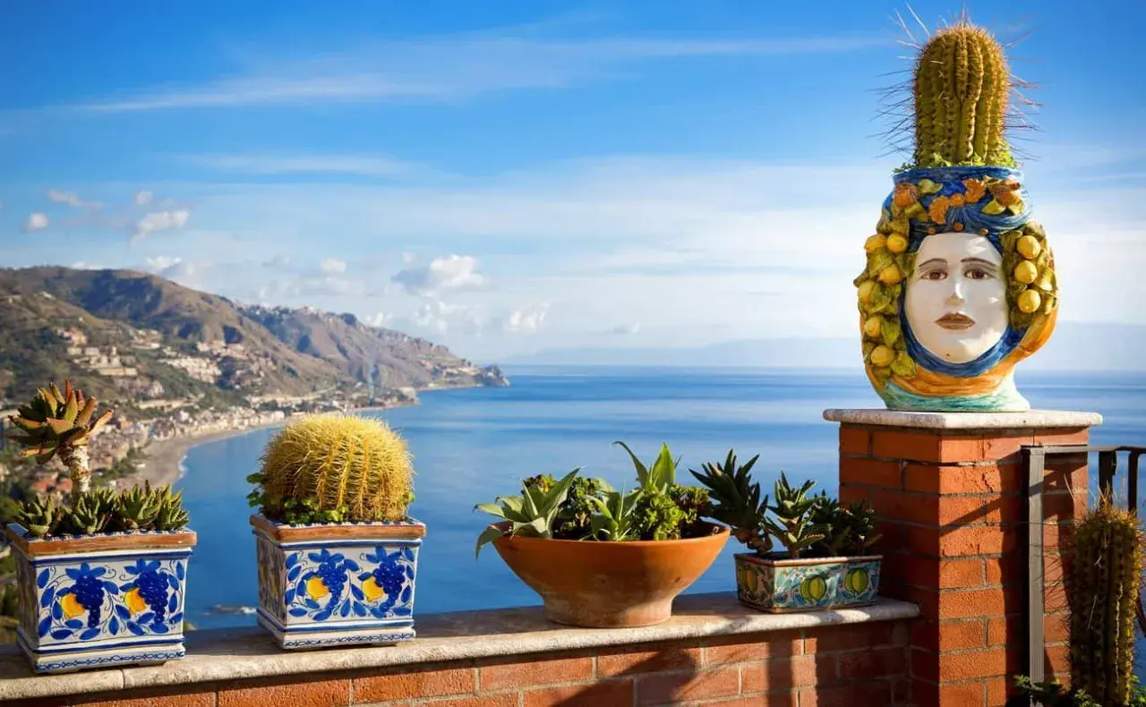 Balcone fiorito con vista sul mare, tra i posti più belli della Sicilia. Cactus e vasi decorati con teste di moro.