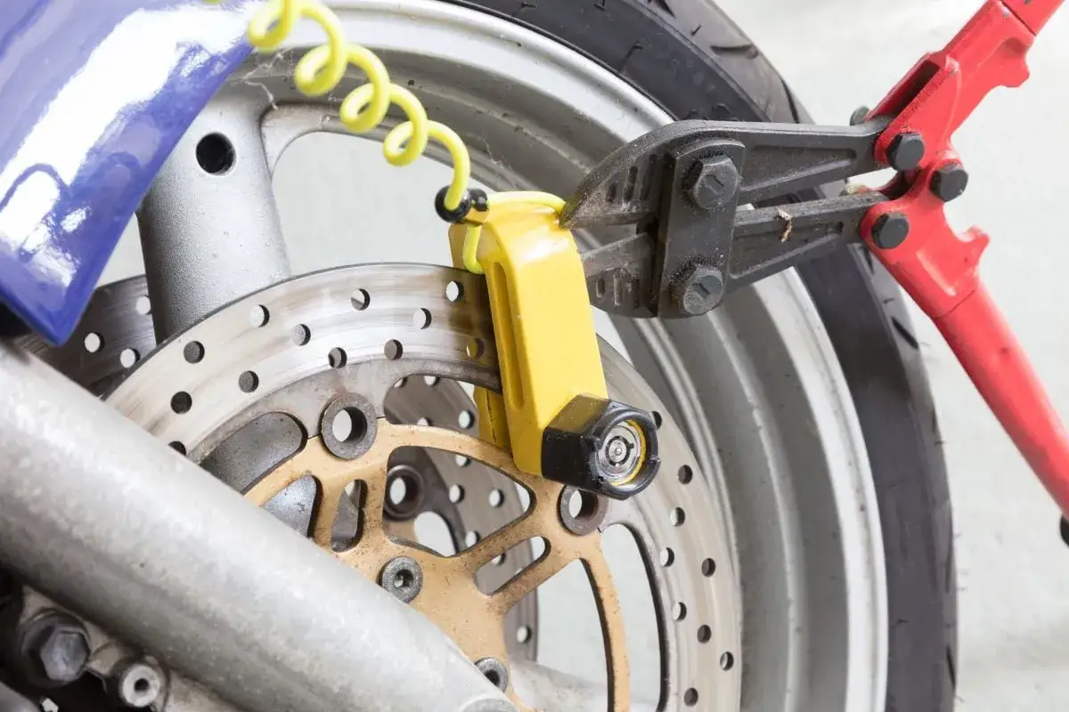 Pinze taglia bulloni rosse tentano di rompere un lucchetto giallo sul disco freno di una moto. Un promemoria che il miglior antifurto meccanico moto &egrave; quello che scoraggia i ladri.