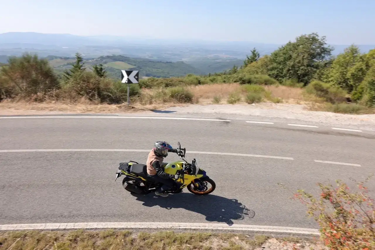 Motociclista in viaggio da Firenze a Siena, attraversa una strada panoramica tra le colline toscane sotto un cielo azzurro.