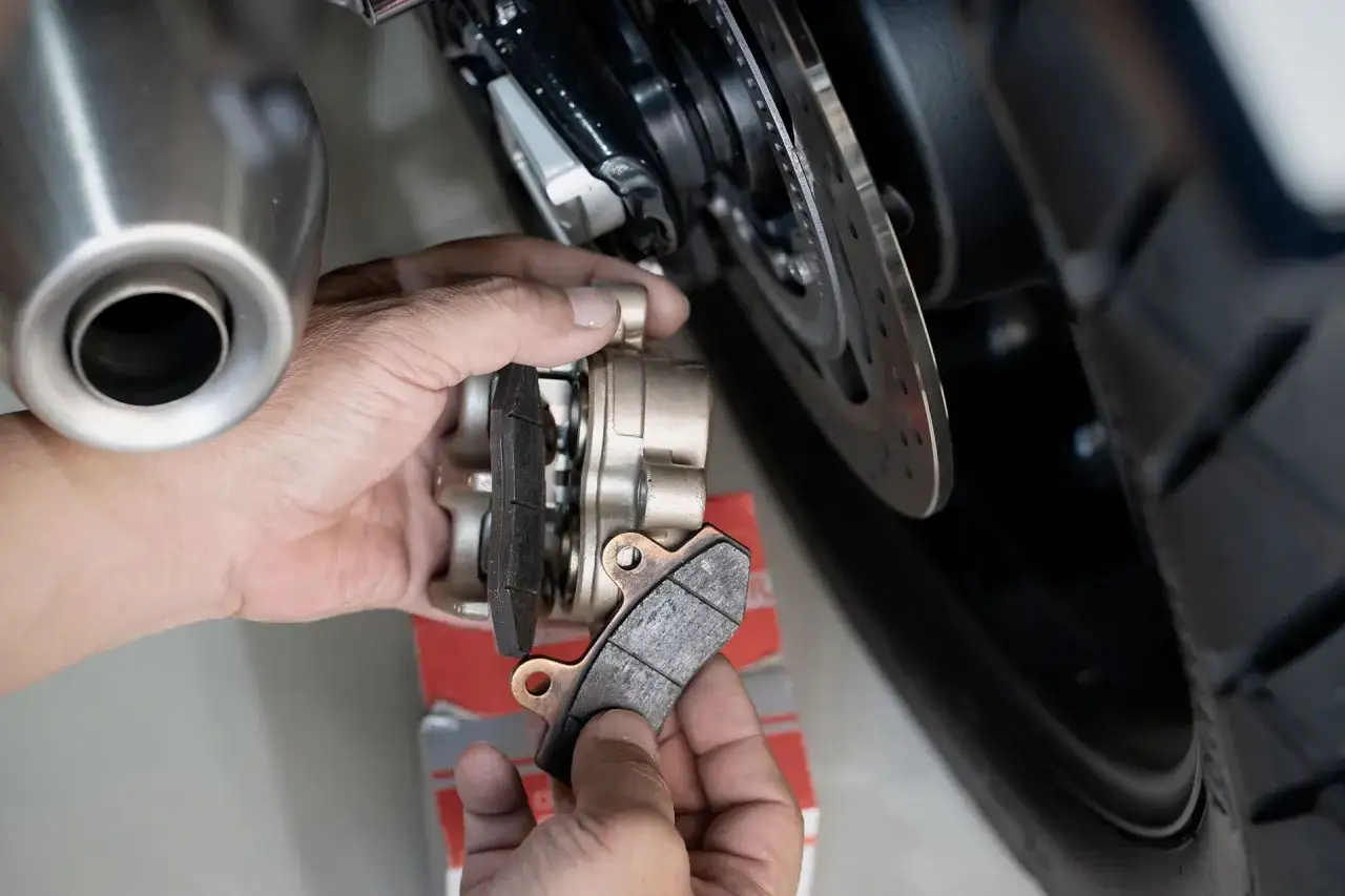 Mano che sostituisce le pastiglie dei freni posteriori di una moto. La durata delle pastiglie freni posteriori è fondamentale per la sicurezza.