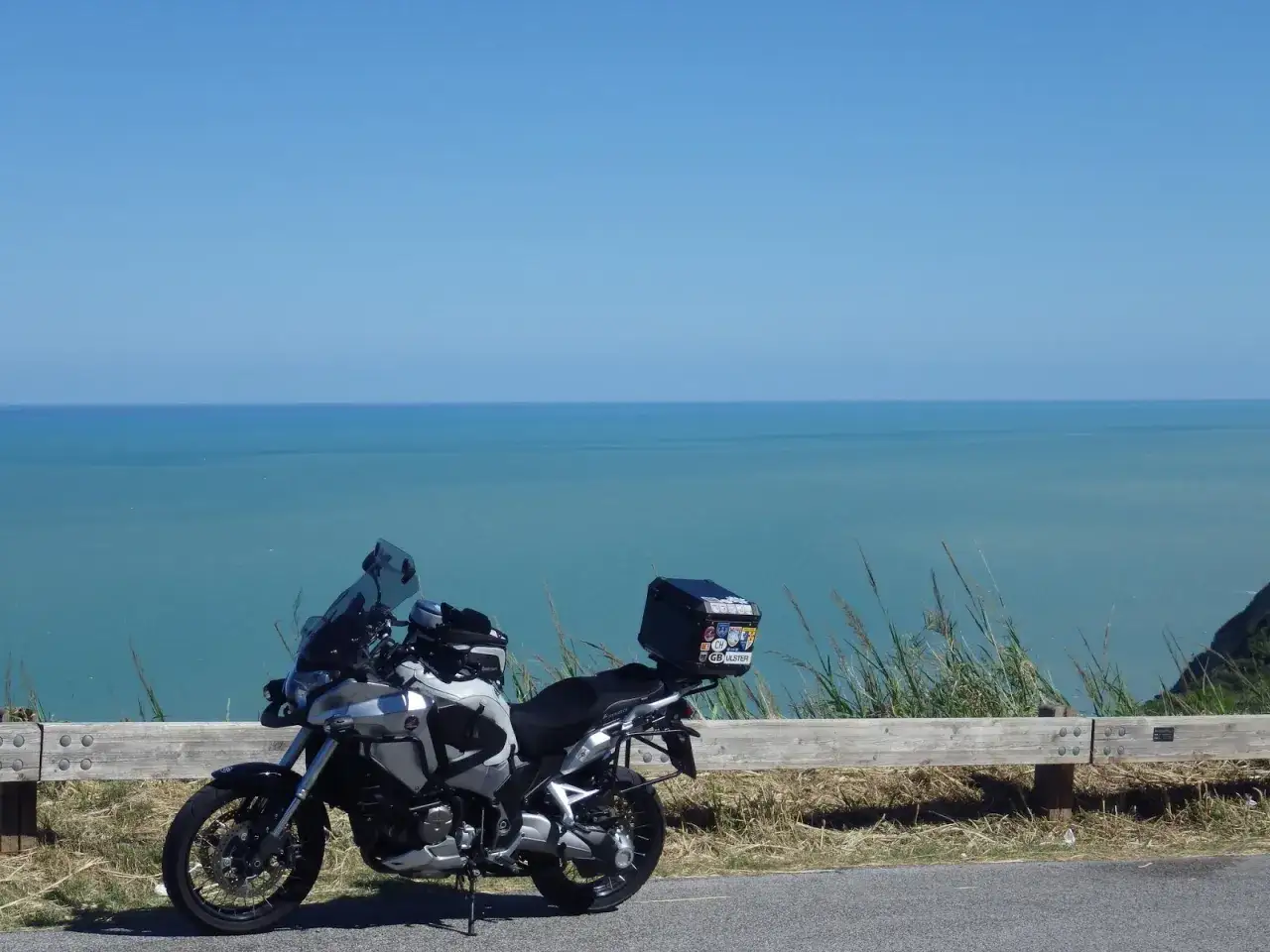 Moto parcheggiata con vista sul mare blu intenso. Un viaggio in moto verso il Conero, con il vento e il profumo del mare.