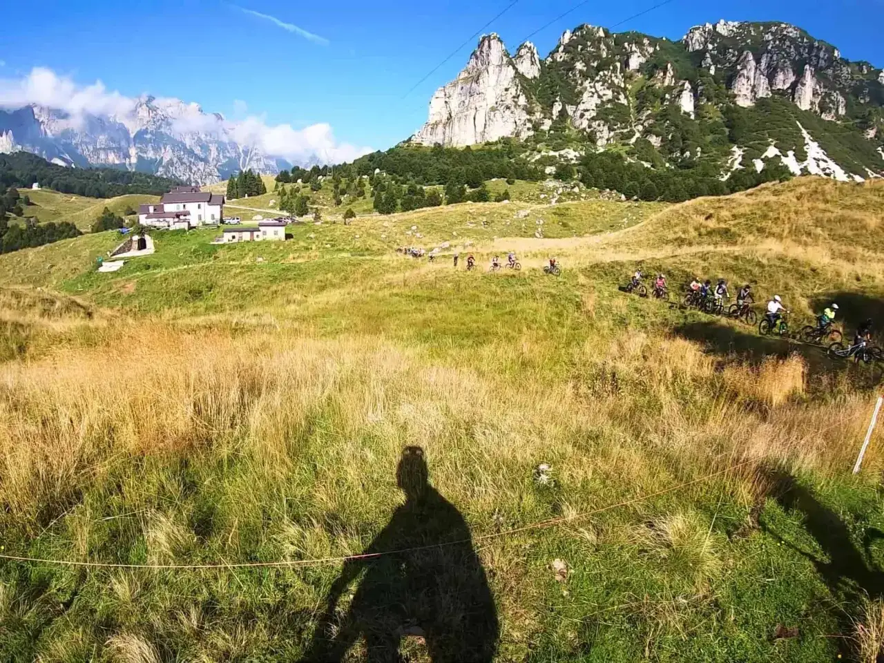 Un gruppo di ciclisti affronta un sentiero erboso con montagne imponenti sullo sfondo, un'avventura a Recoaro 1000.