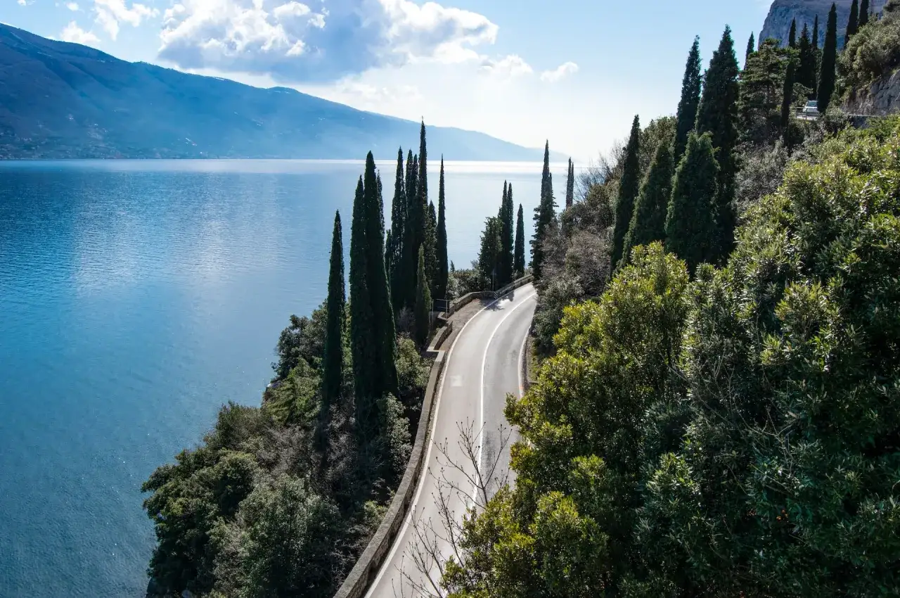 Strada panoramica sul lago, ideale per itinerari moto 2 giorni. Cipressi slanciati e vegetazione rigogliosa accompagnano la curva.