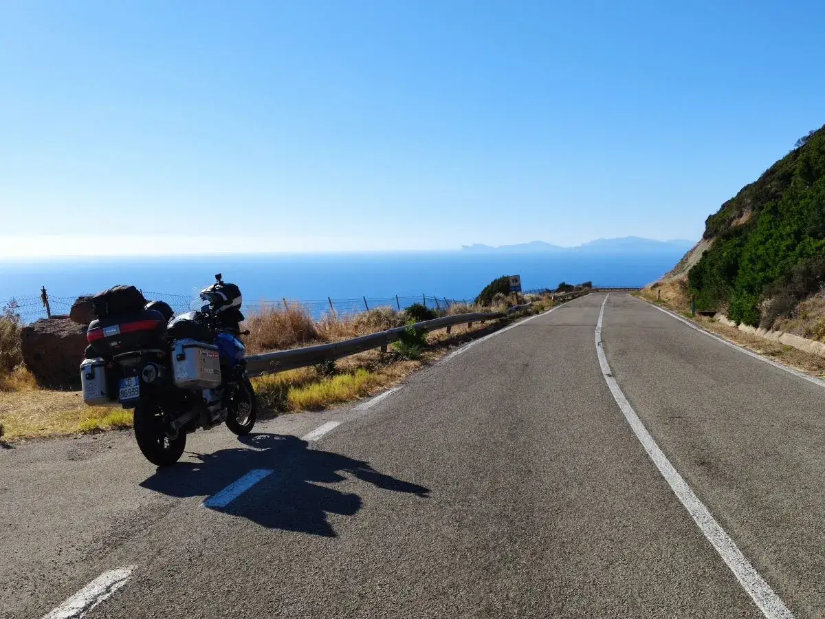 Moto parcheggiata su strada panoramica con mare blu intenso, un viaggio da Cagliari ad Alghero.
