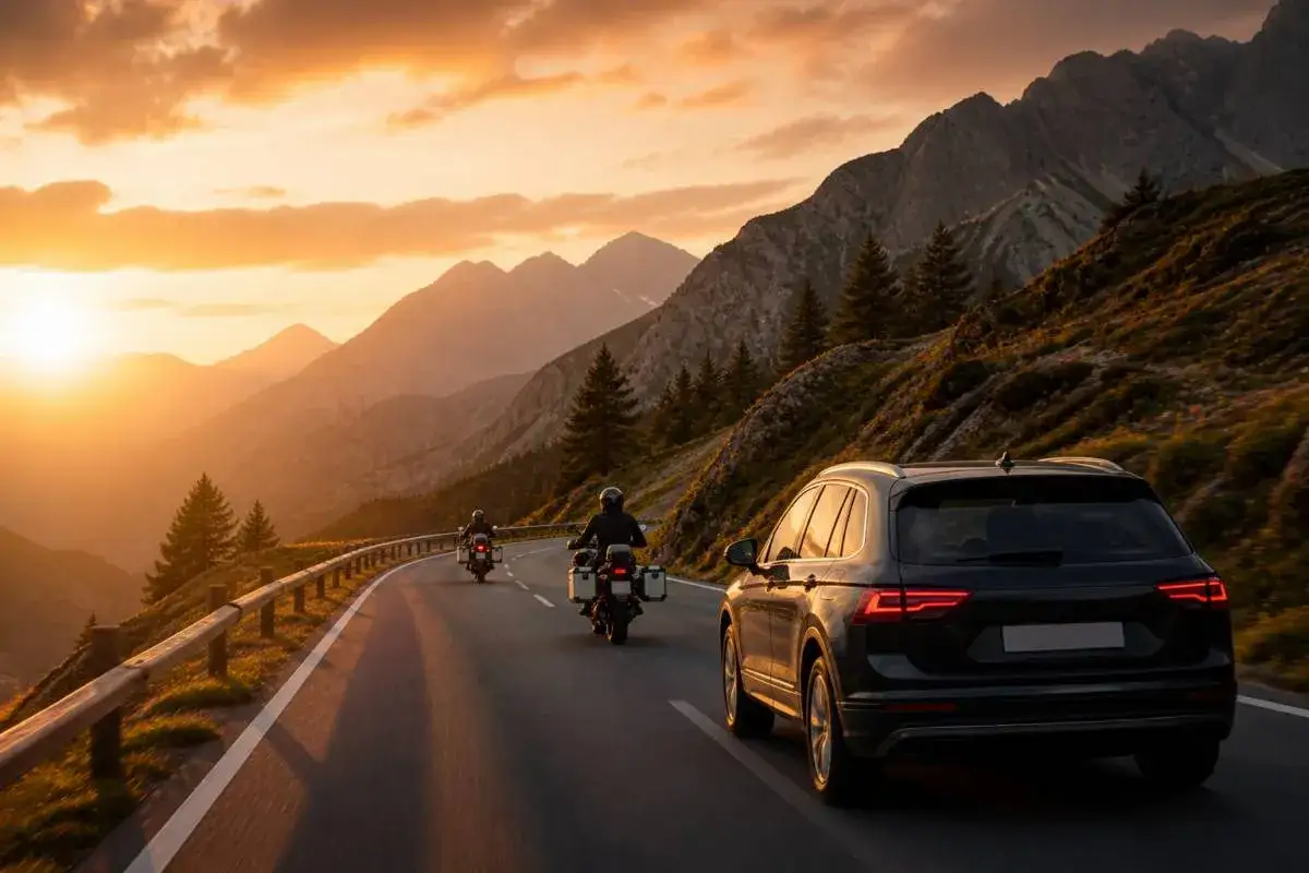 Due motociclisti e un'auto percorrono la SS 439 al tramonto, tra montagne maestose e un cielo infuocato.
