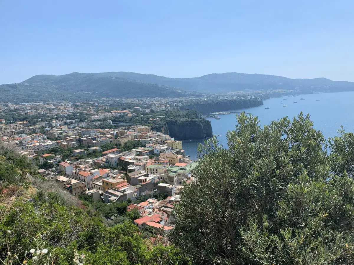 Vista panoramica di Meta di Sorrento con case colorate, il mare blu e colline verdi sullo sfondo.